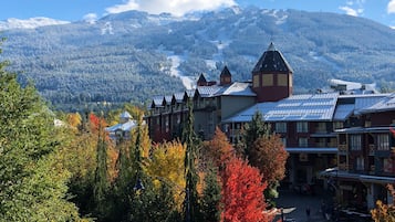 A hotel with a mountain view, featuring a bell tower and a ski slope in the background.