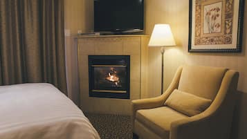 Une chambre d’hôtel avec un lit, une chaise, une cheminée, une télévision et une lampe.
