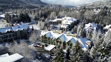 Un albergue con varias construcciones, rodeado de árboles cubiertos de nieve y montañas al fondo.