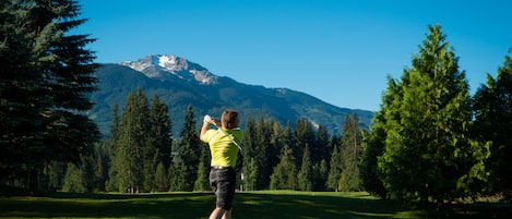 Un campo de golf con montañas al fondo, árboles y cielo despejado.