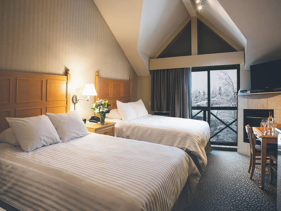 Une chambre d’hôtel avec deux lits, un bureau avec une chaise, une télévision et une cheminée.