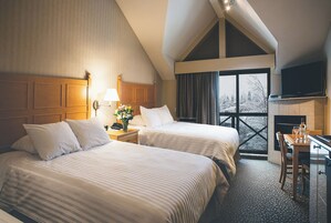 Una habitación de hotel con dos camas, un escritorio con silla, televisión y chimenea.
