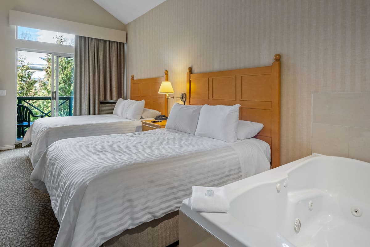 Een hotelkamer met twee bedden, een ruime badkuip en een balkon met uitzicht op groen.