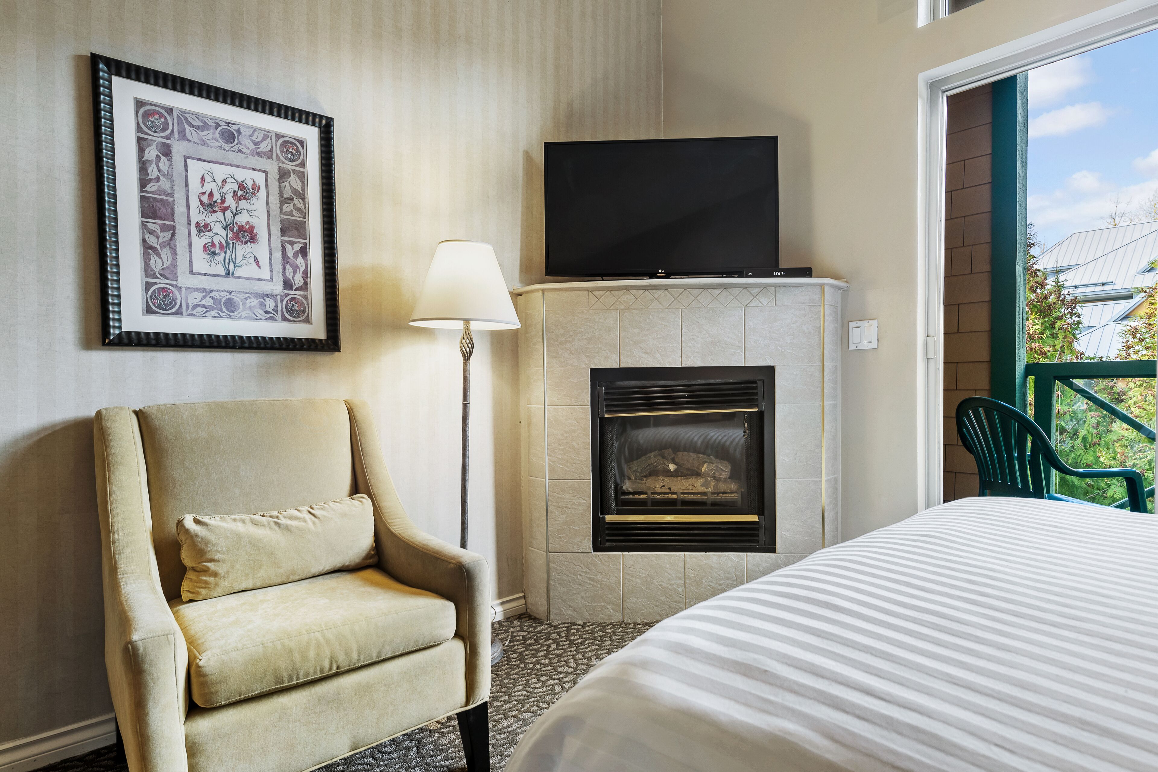 Une chambre d’hôtel avec un lit, une chaise, une cheminée, un téléviseur et un tableau encadré au mur.