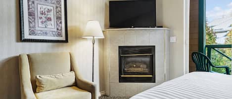 A hotel room with a bed, a chair, a fireplace, a television, and a framed picture on the wall.