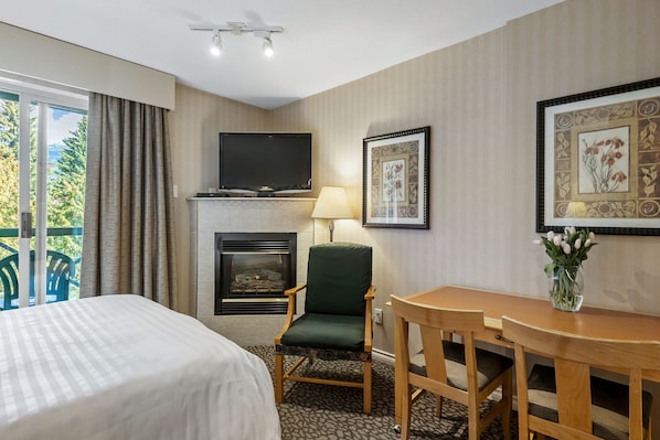A hotel room with a bed, a chair, a table, a fireplace, a TV, and a window with curtains. - Pinnacle Hotel Whistler Village (Whistler)