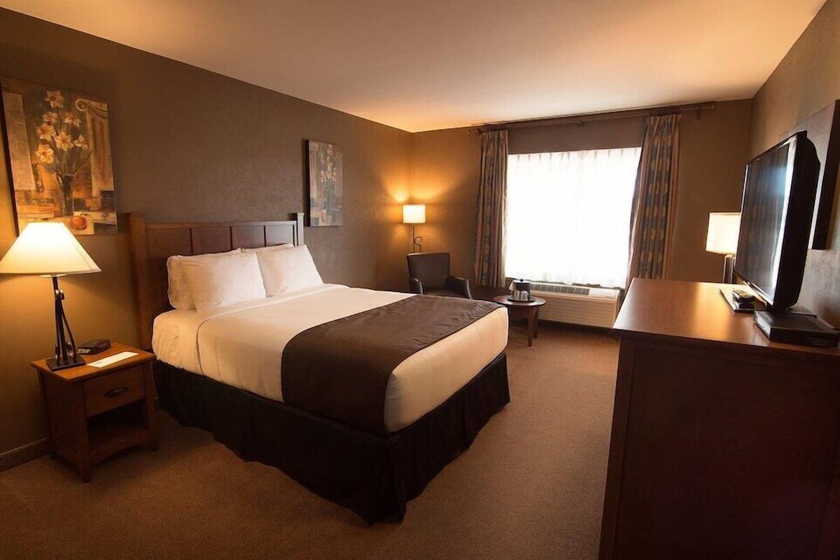 Een hotelkamer met een bed, nachtlampjes, een bureau met een televisie, en een raam met gordijnen.