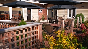 An outdoor patio area with tables and chairs, umbrellas, and a brick wall. - Maritime Inn, an Ascend Collection Hotel (Port Hawkesbury)