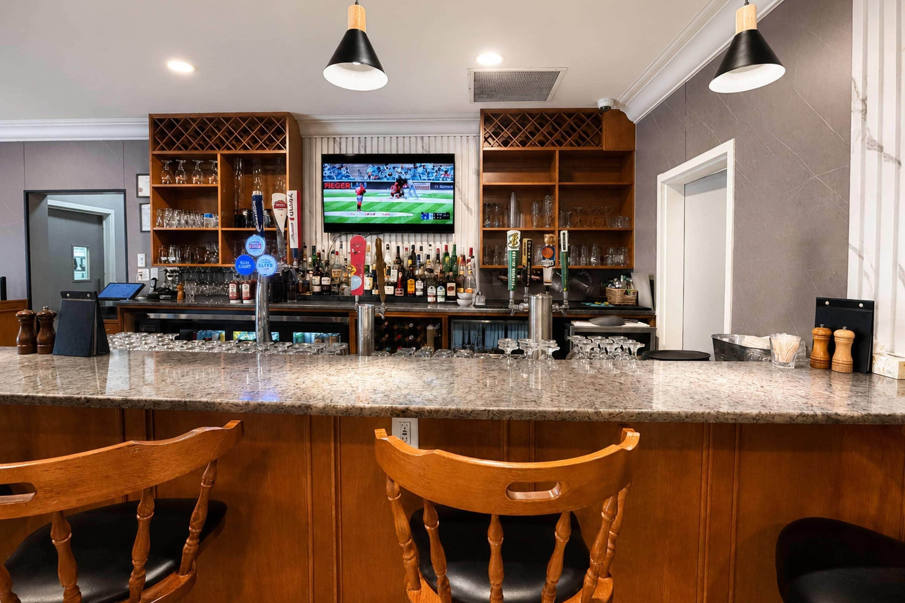 A bar area with a television displaying a sports game, shelves with bottles, and two wooden bar stools.