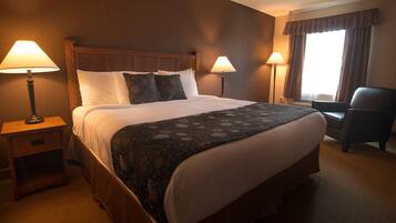 Quarto de hotel com uma cama grande, duas luminárias de cabeceira, uma cadeira e uma janela com cortinas.