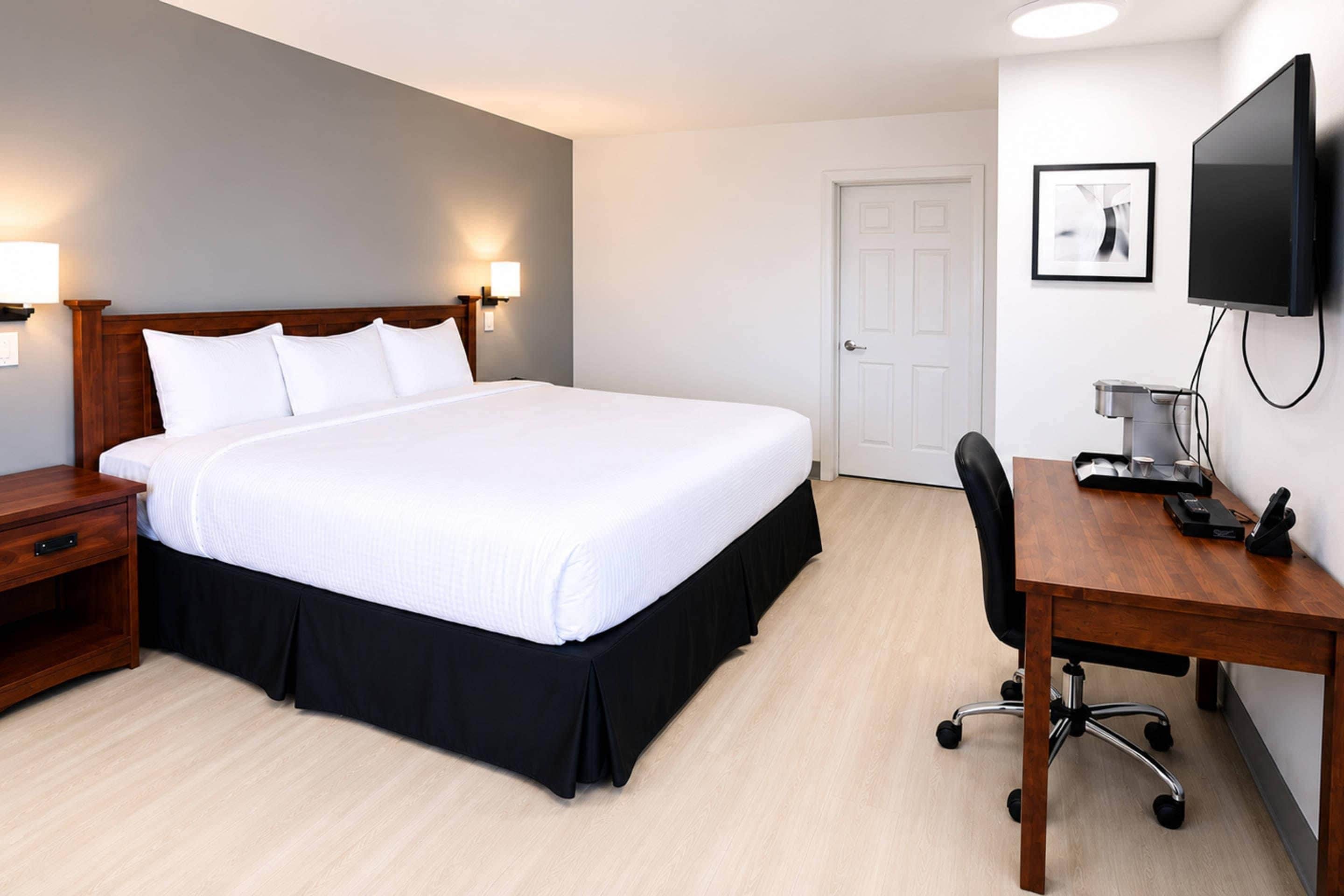 A hotel room with a bed, bedside tables, a desk, a chair, a television, and a door.