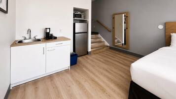 A modern hotel room with a kitchenette, a bed, a mirror, and a staircase.