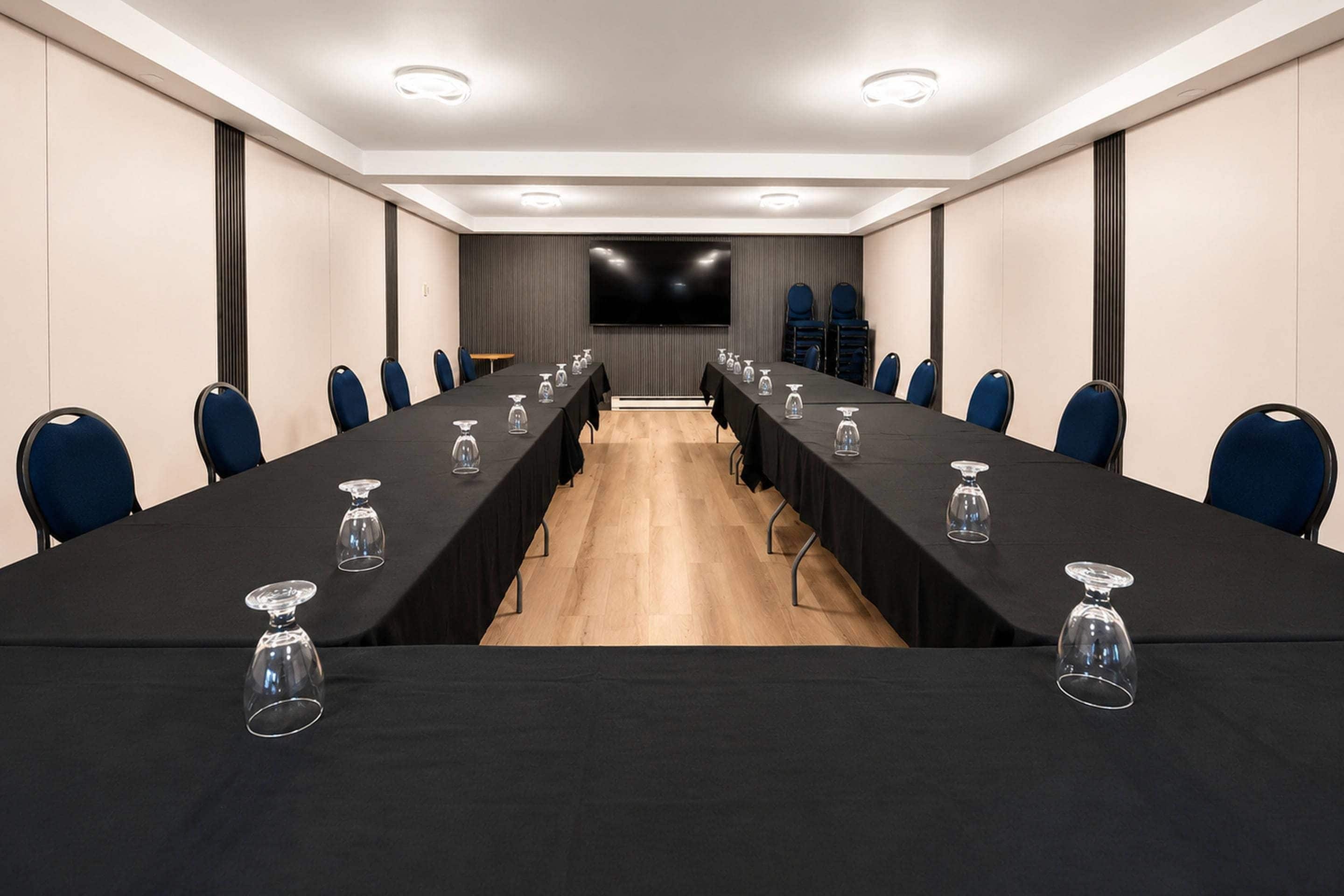 A conference room with a long table, chairs, and a large screen.