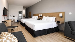 Habitación de hotel con dos camas, un escritorio, una silla, un sofá, un televisor y una kitchenette.