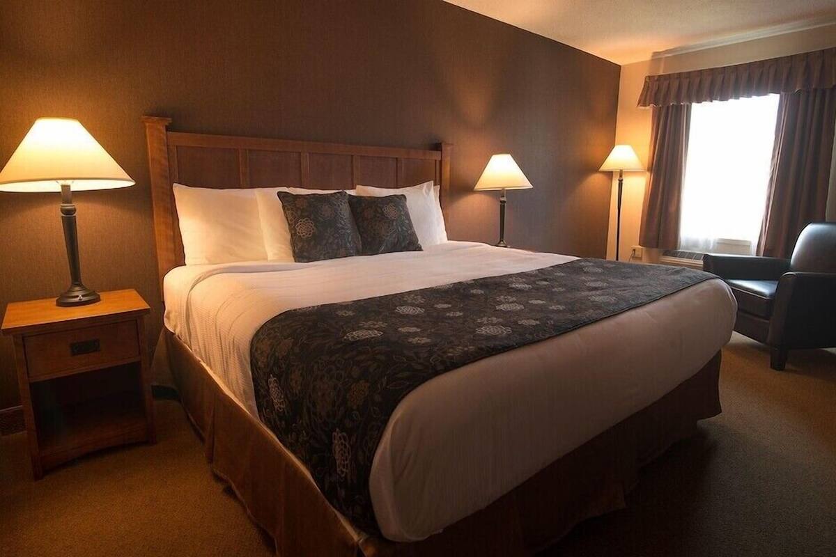 Een hotelkamer met een groot bed, twee bedlampen, een stoel en een raam met gordijnen.