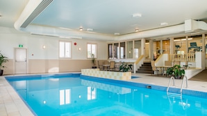 Una piscina interior con agua cristalina, un borde empedrado y una escalera que lleva a un nivel superior.