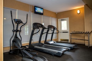 Een fitnessruimte met loopbanden, een hometrainer en een televisiescherm.