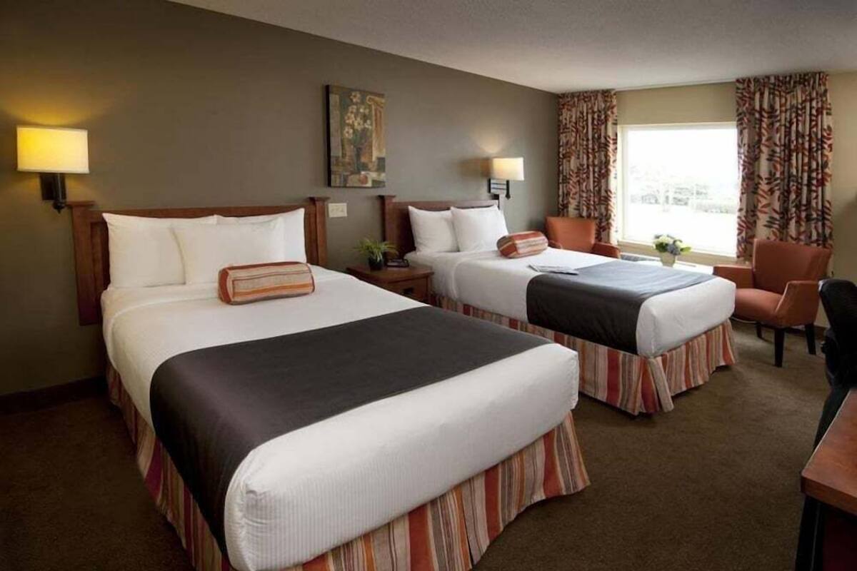 Een hotelkamer met twee bedden, een bureau, een stoel en een raam met gordijnen.