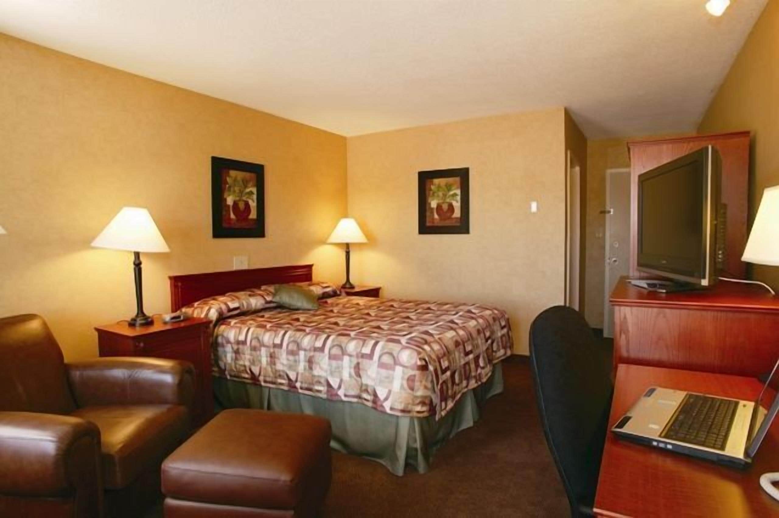 A hotel room with a bed, two bedside tables with lamps, a desk with a laptop, a chair, and a television.