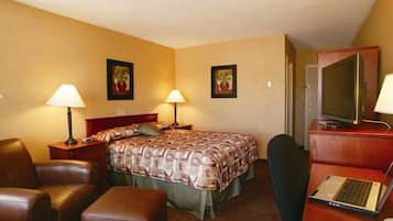 A hotel room with a bed, two bedside tables with lamps, a desk with a laptop, a chair, and a television.
