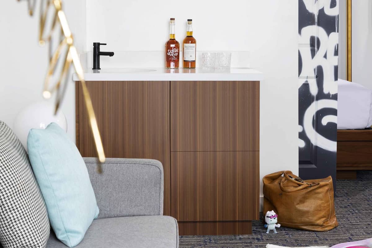 A modern living room with a grey sofa, a wooden cabinet, and a small table with two bottles of liquor and glasses.