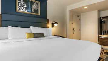 A hotel room with a large bed, a framed artwork on the wall, a bedside lamp, and a door leading to a bathroom.