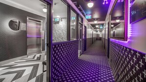 A hallway with patterned flooring, a mirrored wall, and an elevator. - Hotel Belmont Vancouver - MGallery Collection (Vancouver)