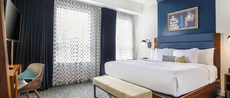 Una habitación de hotel con una cama grande, un banco, un escritorio con una silla y un televisor.