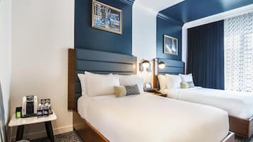 Hotelkamer met twee bedden, een nachtkastje met telefoon en koffiezetapparaat, en een klein tafeltje met prullenbak en waterfles.