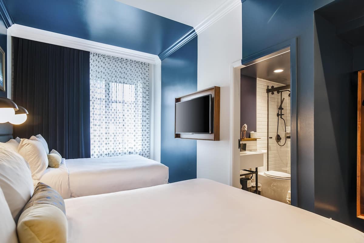 A hotel room with a bed, a TV, a window with curtains, and a shower area.