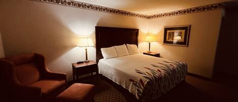 A hotel room with a bed, two bedside tables with lamps, a chair, and a framed picture on the wall.