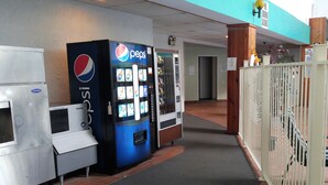 A hallway with vending machines, including a Pepsi cooler, and a gated area with a pool sign.