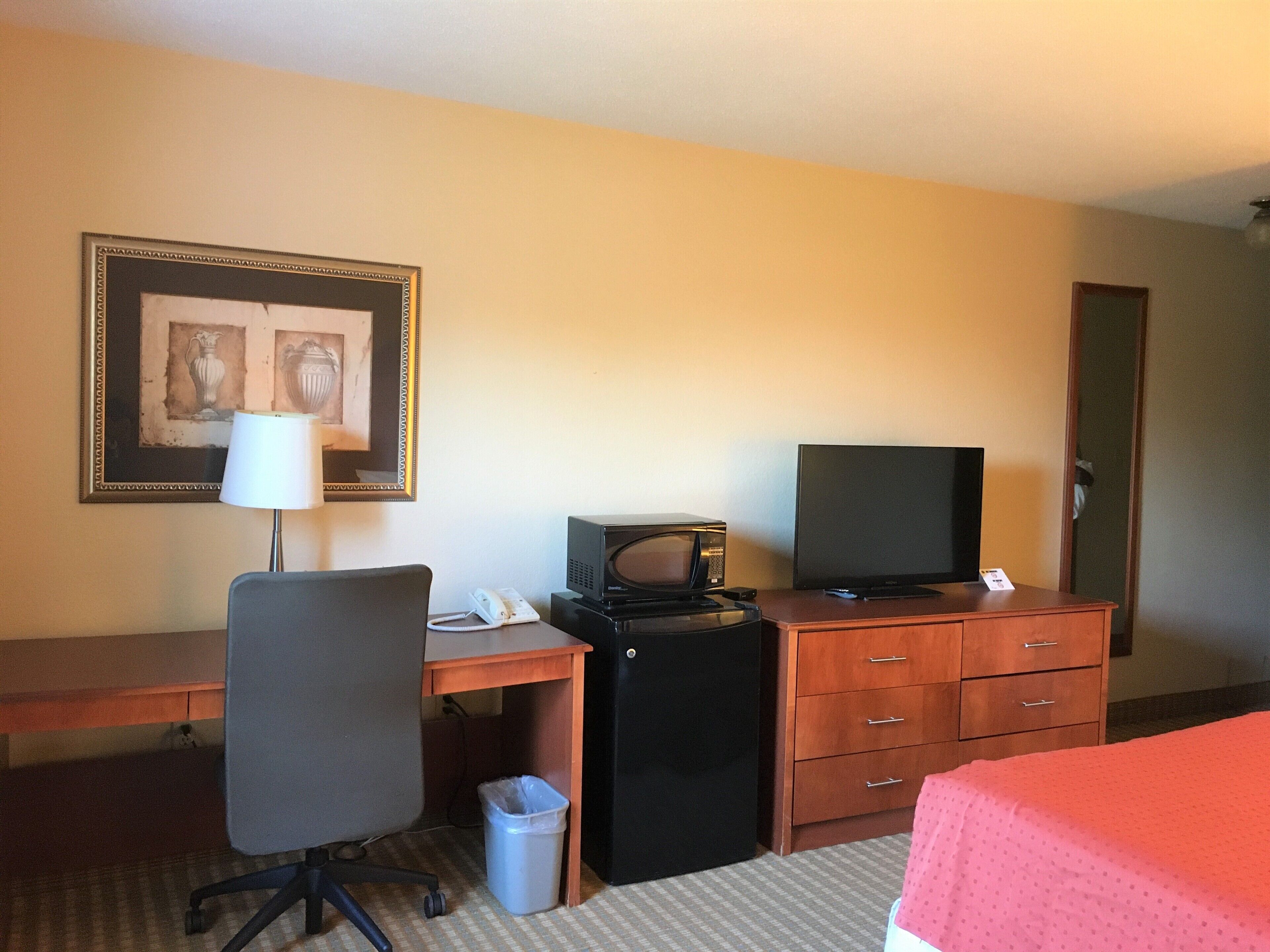 A hotel room with a desk, chair, television, and a bed.