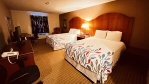 A hotel room with two beds, a desk, a chair, a lamp, and a window with curtains.