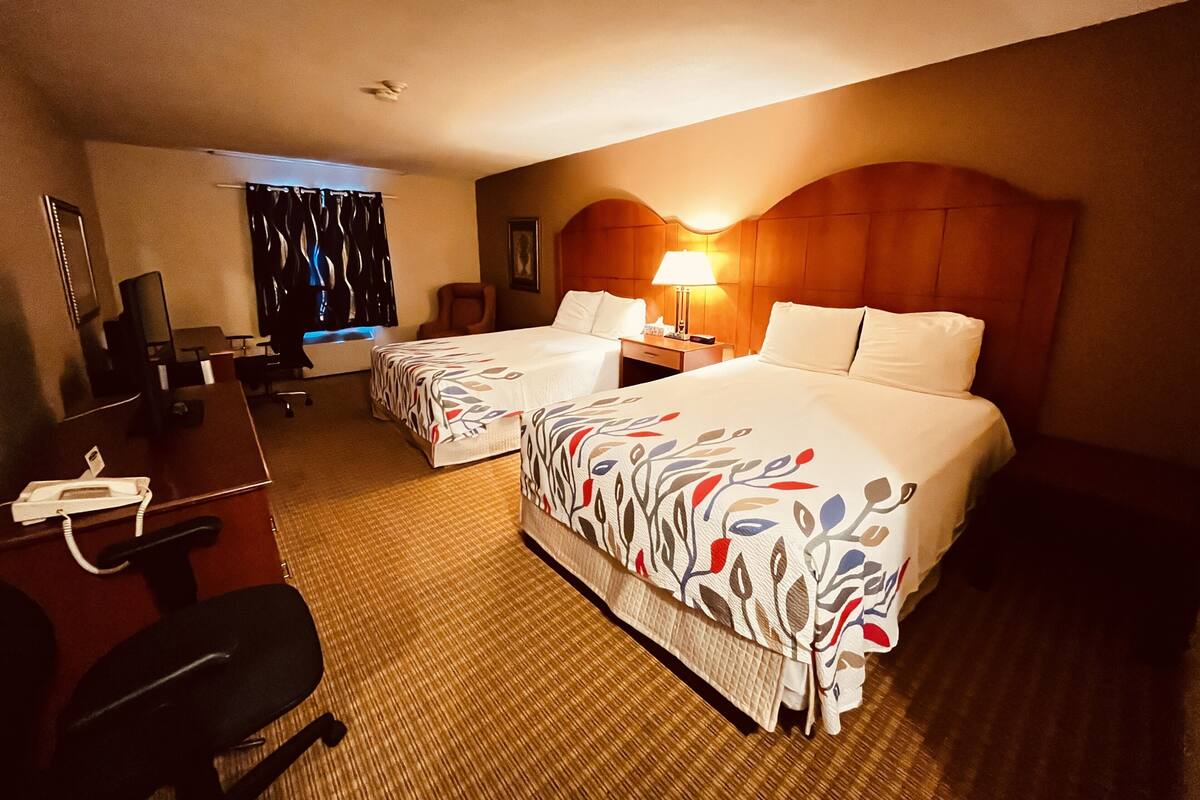 Habitación de hotel con dos camas, un escritorio, una silla, una lámpara y una ventana con cortinas.