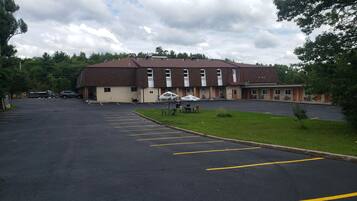 A parking lot with a building that has multiple windows and a covered area with tables and chairs.
