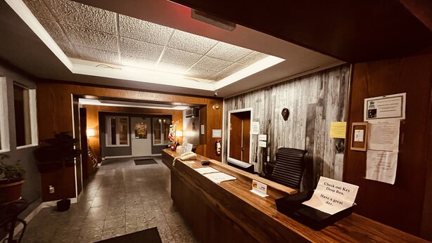 A hotel reception area with a wooden reception desk, a black office chair, a large window, and a sign instructing to check out the key drop box.