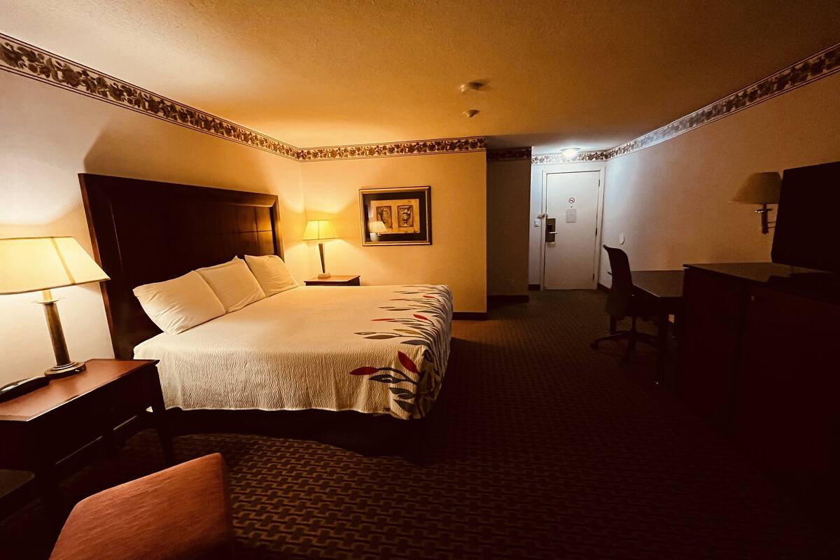 Habitación de hotel con una cama grande, un escritorio, una silla, un televisor y una puerta.