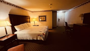 Habitación de hotel con una cama grande, un escritorio, una silla, un televisor y una puerta.
