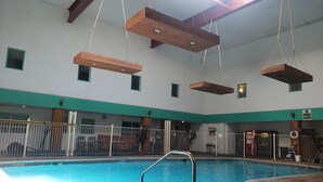 An indoor swimming pool with a clear water surface, surrounded by a white poolside area with a metal ladder.