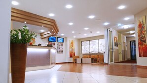 A hotel reception area with a wooden reception desk, two monitors, a large window with a view of a building, and a potted plant. - Central Hotel Löwen (Feldkirch)