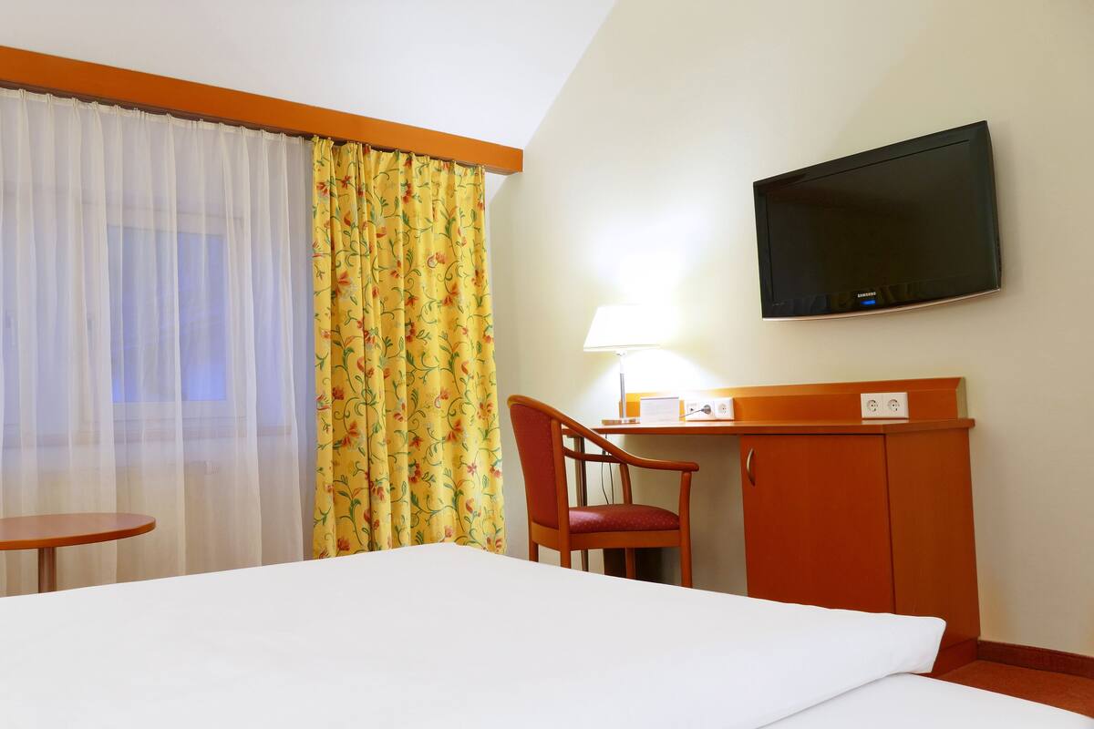 A hotel room with a bed, a desk, a chair, a television, and curtains.