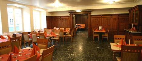 A dining area with multiple tables and chairs, wooden paneling on the walls, and a marble floor.