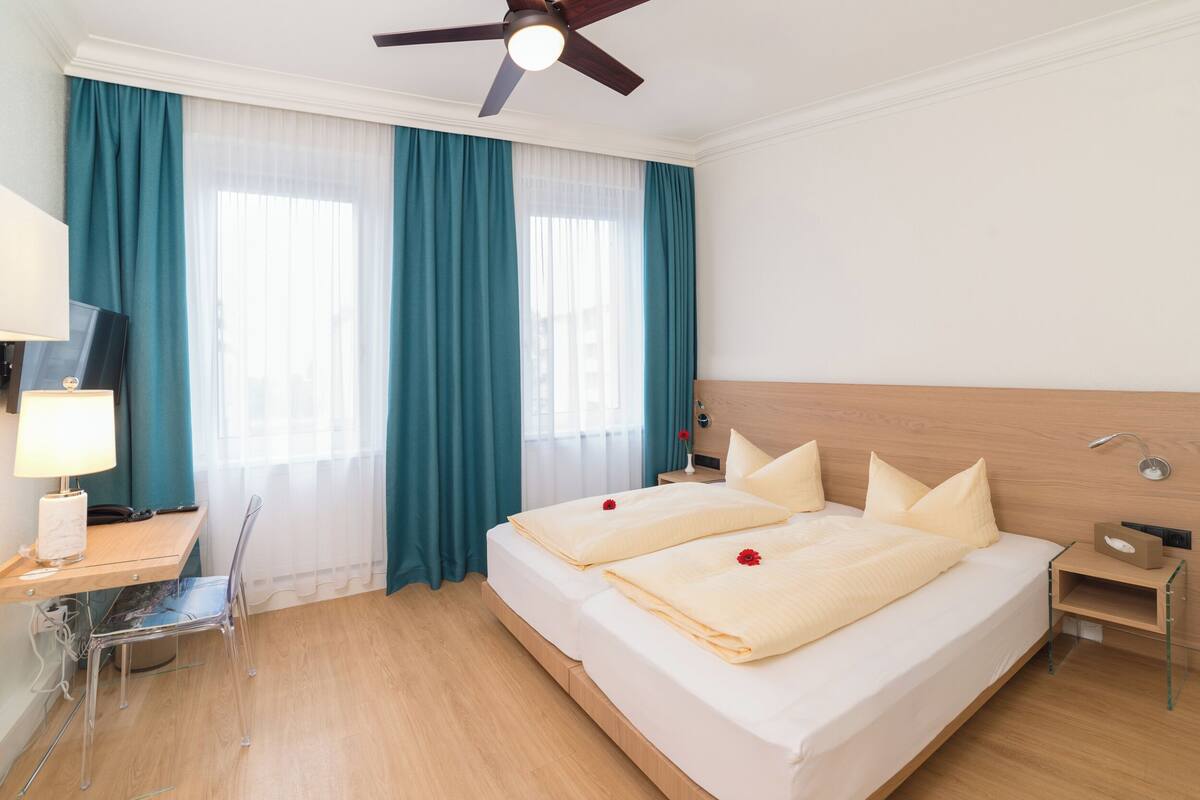 A hotel room with a bed, a desk, a chair, a TV, and a ceiling fan.