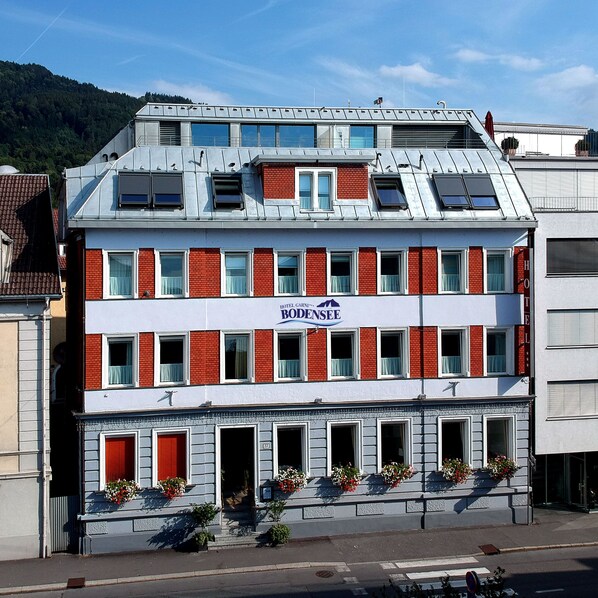 A hotel with a red and white facade, multiple windows, and flower boxes on the ground floor. - Hotel Bodensee Bregenz (Bregenz)