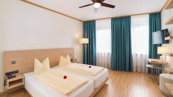 Ein Hotelzimmer mit zwei Betten, einem Schreibtisch mit Stuhl, einem Fernseher und einem Deckenventilator.