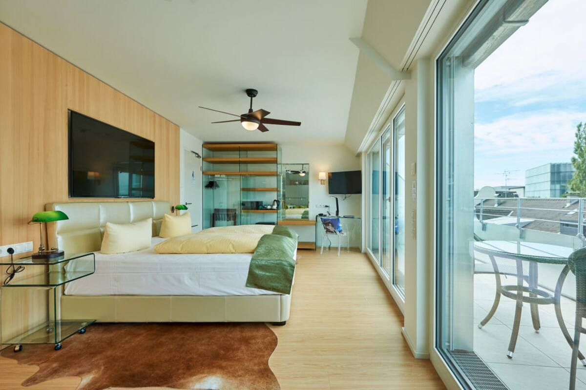 A modern bedroom with a bed, a desk, and a large window.