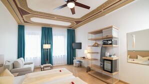 Ein Hotelzimmer mit einem Bett, einem Fernseher, einem Deckenventilator, einer Glasvitrine und einem Spiegel.