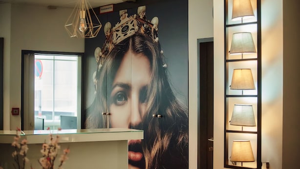 Una zona de recepción con un mostrador de vidrio, una corona decorativa en la pared y varios apliques.
