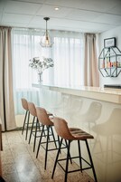 Een moderne bar met een glazen toonbank, barstoelen en een hanglamp.